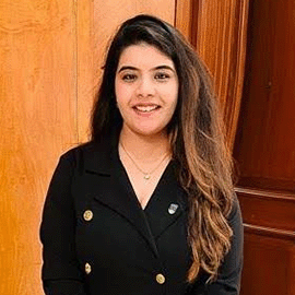 A smiling woman wearing a black blazer looks directly ahead.